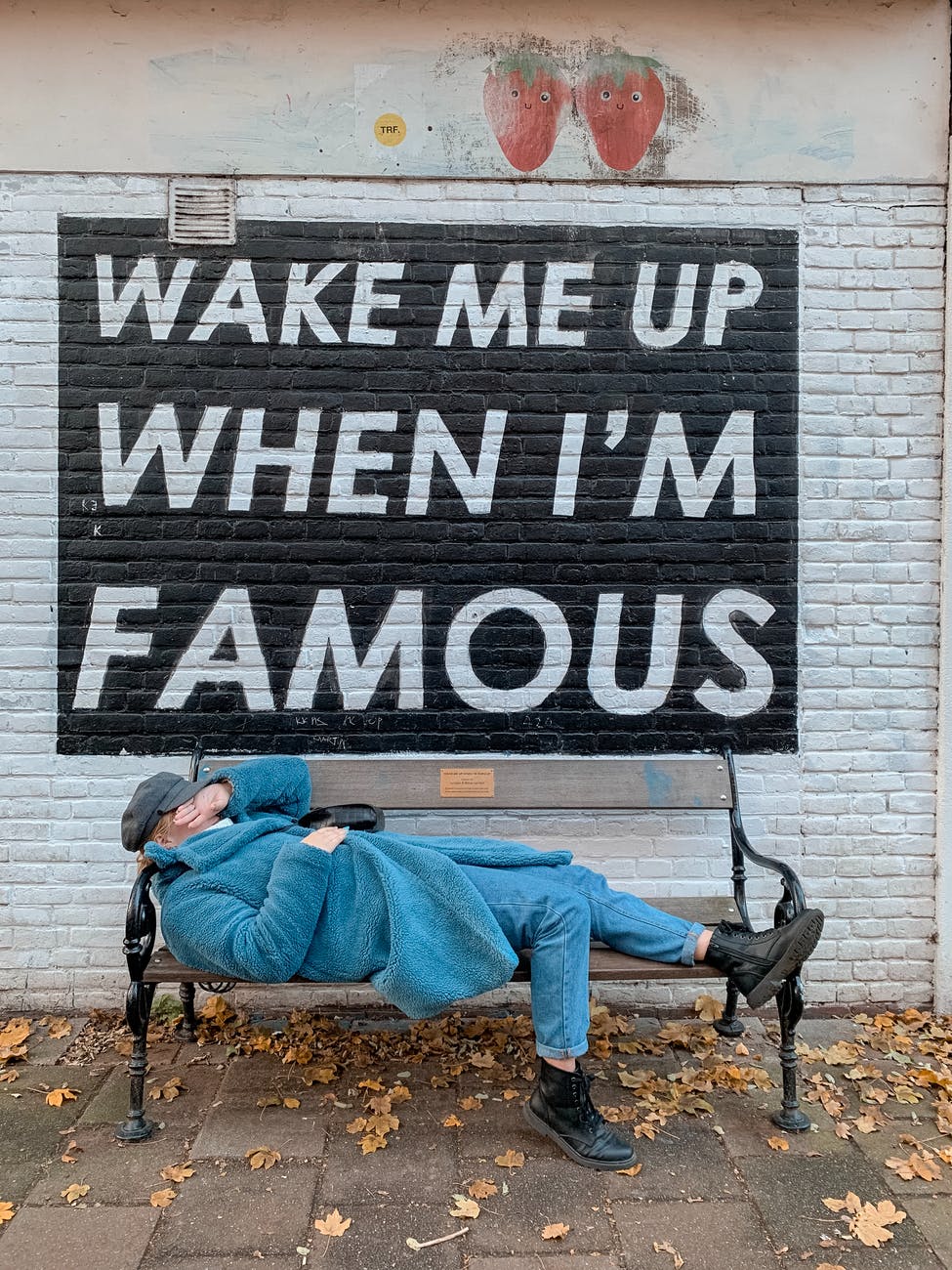 unrecognizable trendy woman lying on street bench near wall with inscription on autumn day