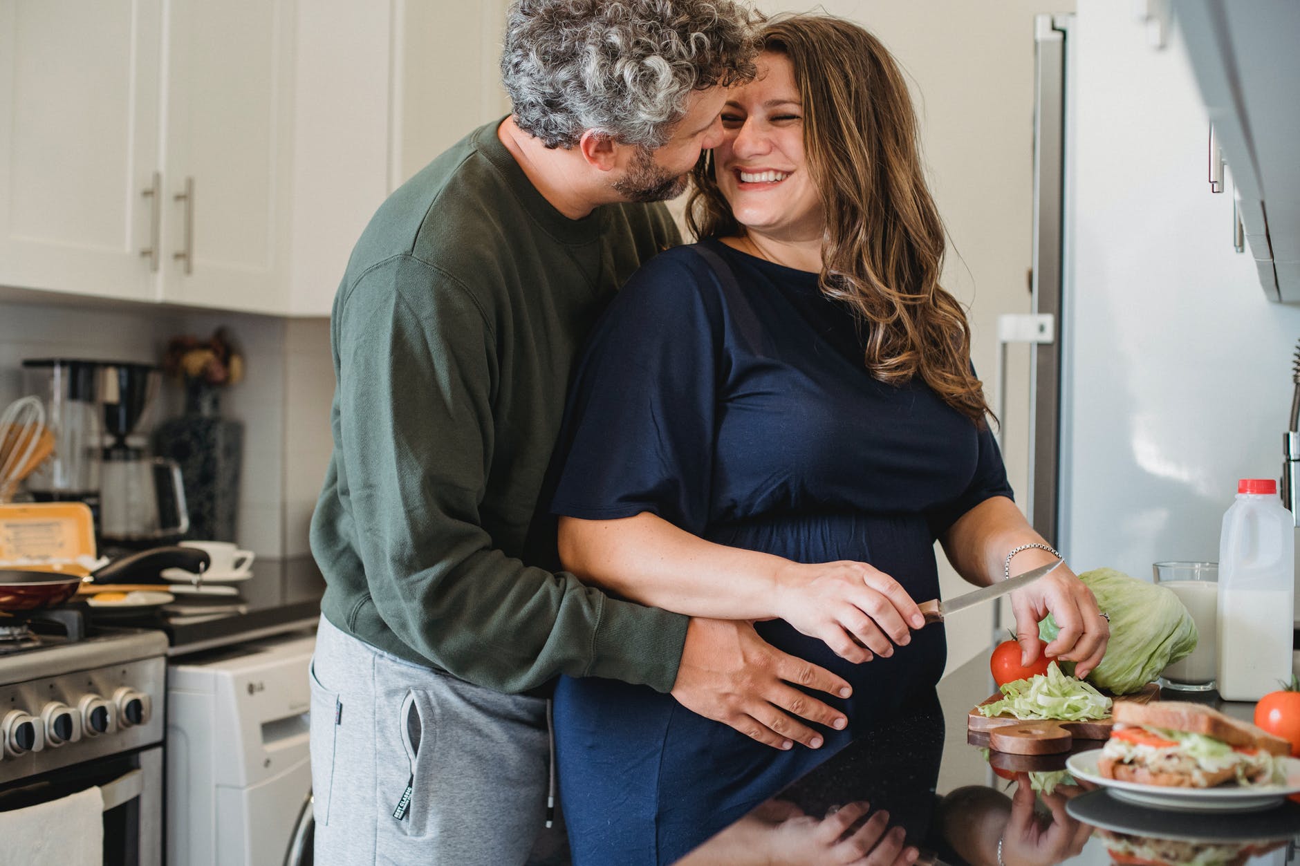 loving husband embracing pregnant wife while cooking sandwiches