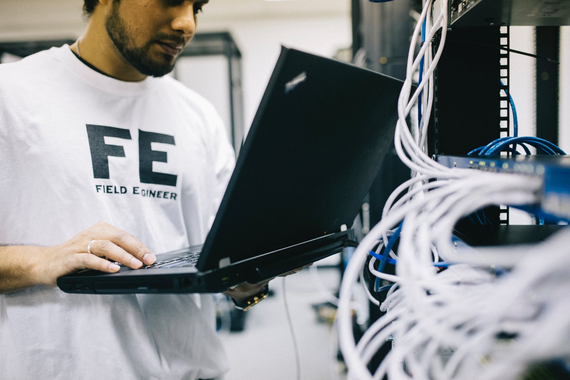 serious ethnic field engineer examining hardware and working on laptop