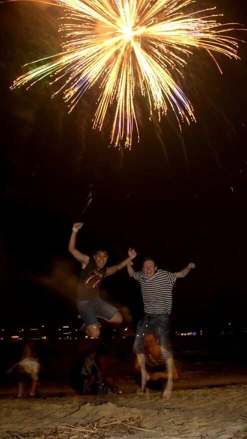 A group of people jumping in the air with fireworks in the background Description automatically generated with medium confidence